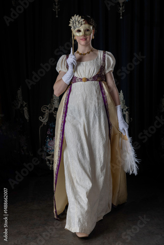 A Regency woman wearing evening attire and holding an ostrich feather fan and a masquerade mask