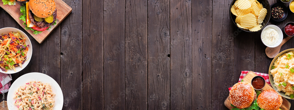 Obraz premium BBQ double border with hamburgers, classic salads and snacks. Above view table scene over a dark wood banner background. Copy space.