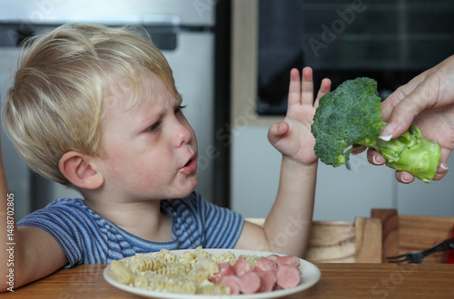 Fotografie portrait of cute toddler sitting at the table with plate with noodles and sausag
