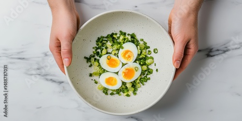 A bowl with soft-boiled eggs and chopped green onions is held by two hands over a marble surface.