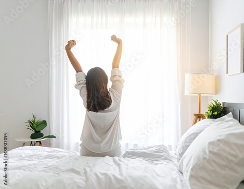 Wallpaper Mural Woman stretching in white hoodie on bed with bright window background and small table with plants. Bright natural light and cozy interior with white and green colors. Torontodigital.ca