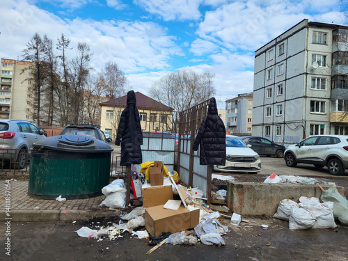 Bilde på lerret Garbage is piled up, two coats are hanging on the fence past the waste containers
