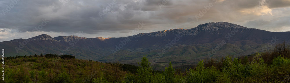 Obraz premium Mountain peaks in the woods landscape. Panoramic view of Suva Plnina mountain range in Serbia. Panoramic photo. Panorama of the mountain range. Sunset and beautiful clouds cover the mountain range. 