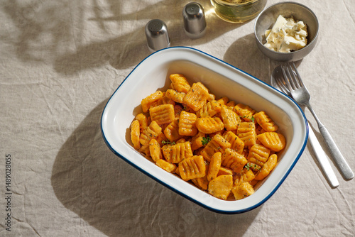 pumpkin gnocchi, garnished with fresh herbs in Enamel Bowl with Cutlery on Linen Tablecloth