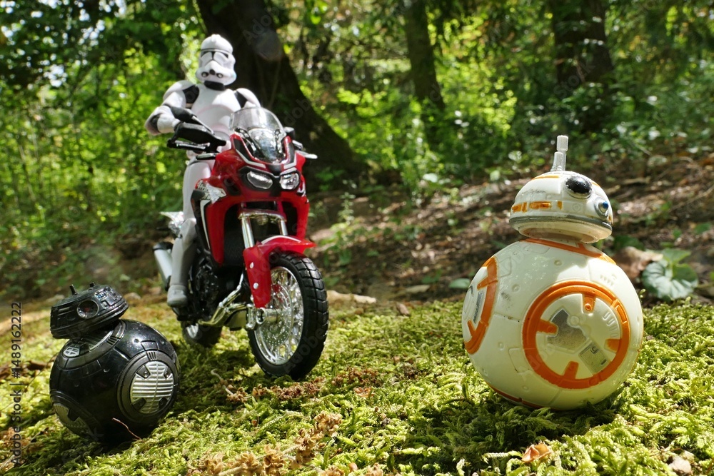 Naklejka premium Star Wars action figure of Clone Trooper, following two ball shaped astromech droids, imperial BB-9E and BB-8 rolling on forest moss in front of him on Honda Africa Twin red dual sport motorbike model