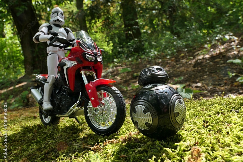 Naklejka premium Star Wars articulated action figure of Clone Trooper riding on dual sport japanese motorbike Honda Africa Twin, chasing black ball shaped imperial droid BB-9E.