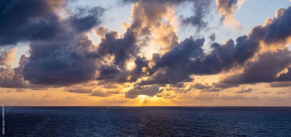 Fototapeta premium Dramatic Sunset Over Ocean with Luminous Clouds and Golden Sky