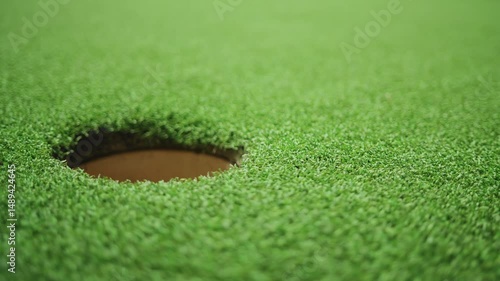 Golf ball rolling toward hole on green grass in slow motion