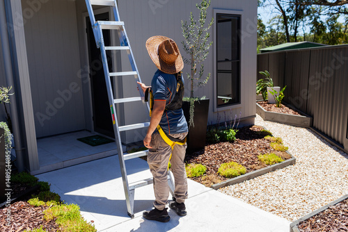 Electrician tradie man stabilising ladder to roof of small suburban house