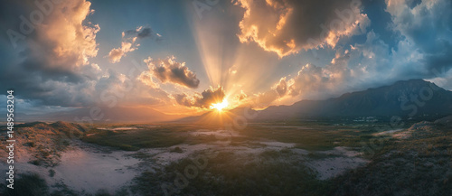 A photo capturing the golden rays of the sun shining through a cloudy sky as it sets over a majestic mountain range.