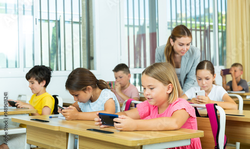 Group of schoolchilds using smartphones while working in classroom during lesson in primary school