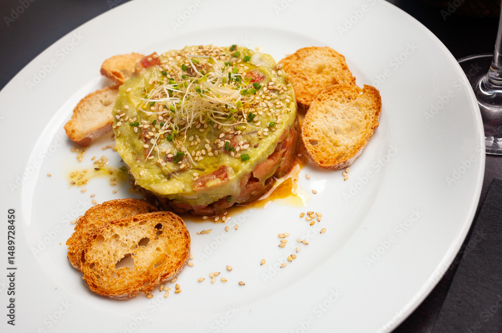 Raw salmon tartare with guacamole, microgreens and sesame seeds served with toasted bread Raw salmon tartare with guacamole, microgreens and sesame seeds served with toasted bread