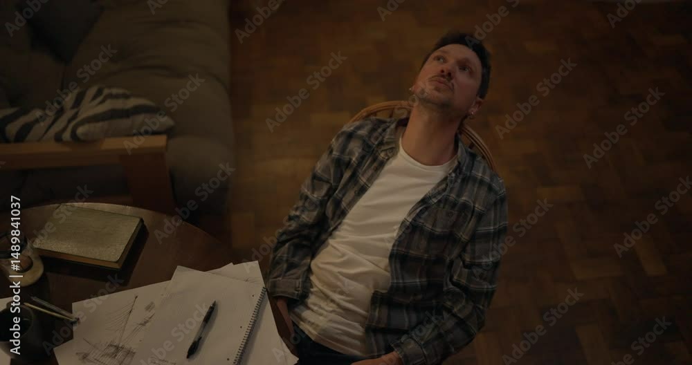 Top view of male writer leaning back in chair at desk and looking up thoughtfully while searching for inspiration for his next work in modern cozy studio Top view of male writer leaning back in chair at desk and looking up thoughtfully while searching for inspiration for his next work in modern cozy studio