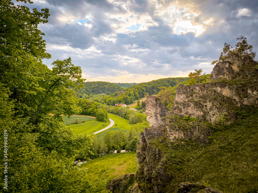 Obraz premium Rock Climbing Area Labertalwand In The Bavarian Jura: Dramatic Limestone Cliff Surrounded By Lush Green Forest And Rolling Meadows Under A Cloudy Spring Sky In Southern Germany