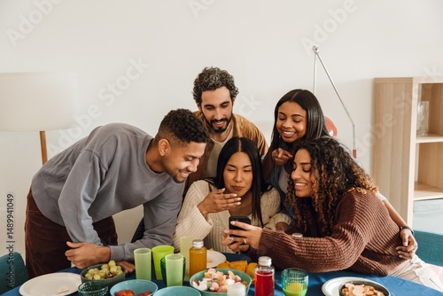 Εκτύπωση καμβά A diverse group of multiracial friends gather indoors around a table, looking at a smartphone and smiling