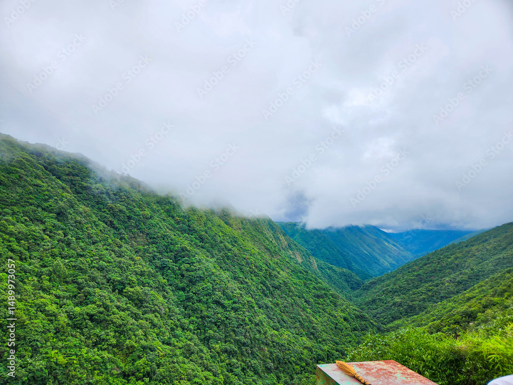 Obraz premium Lush green mountain valley under a cloudy sky with fog rolling through the hills