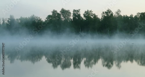 Calm lake at dawn with gentle mist and soft blue tones, creating a serene and peaceful atmosphere.