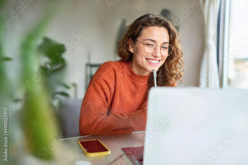 Happy young woman using laptop sitting at desk writing notes while watching webinar, studying online, looking at pc screen learning web classes or having virtual call meeting remote working from home.