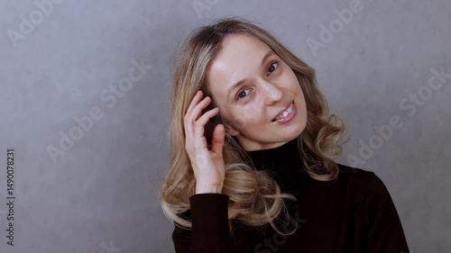 Young woman with blonde hair smiling on gray background, looking at camera, close up, copy space
