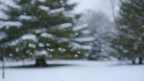 Gentle snowfall against blurred green evergreen trees in a soft winter landscape, serene and calming atmosphere with falling snowflakes