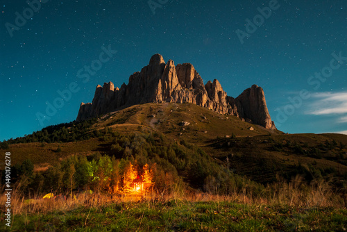 Rocky mountain against the background of the night starry sky. Bonfire at the foot of the mountain