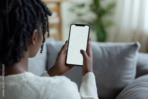 Over shoulder view of gen z African American teen holding smartphone mock up white cell screen template advertising mobile application, watching social media videos on cellphone at home on