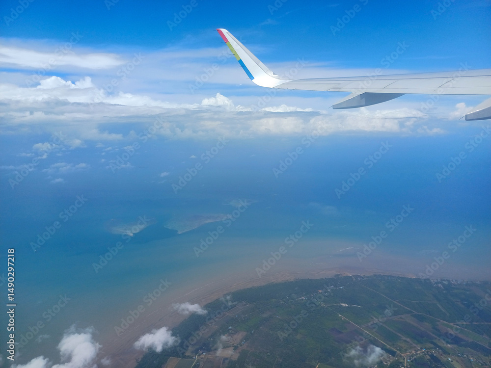 Obraz premium From an airplane window, a view of Indonesia unfolds. Islands are scattered across the turquoise sea, with a patchwork of green rice paddies and coastal villages visible below, provides perspective
