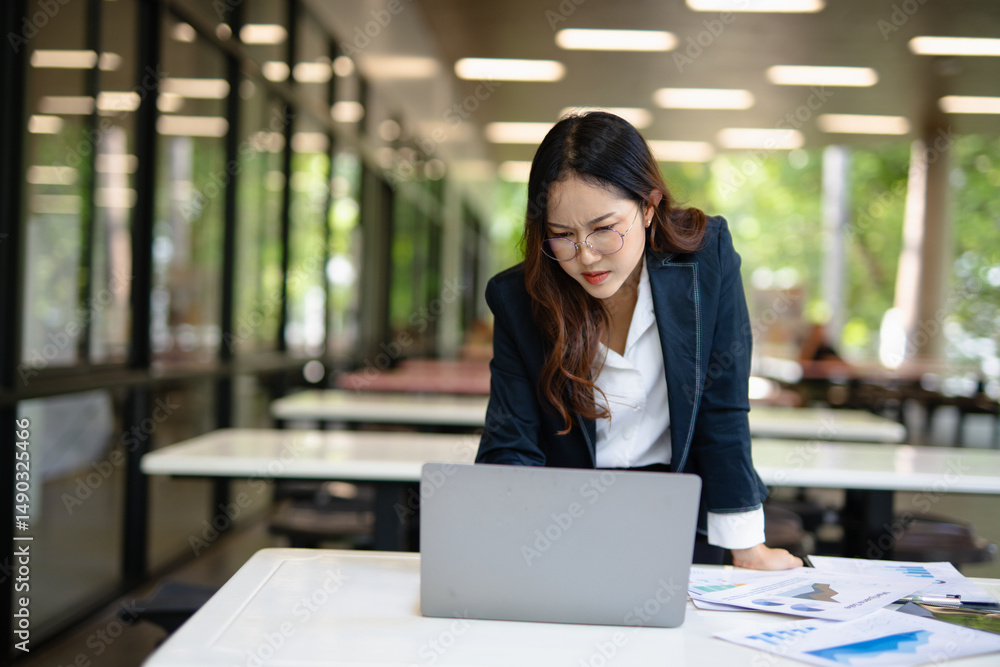 Obraz premium Asian businesswoman working on financial market research using laptop and digital tablet, stressed about digital investment in office.