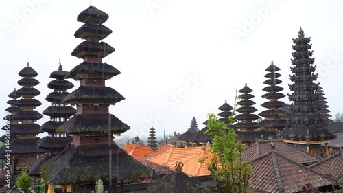 Pura Besakih, Bali’s famous Mother Temple, with tall, multi-tiered meru towers under a misty sky, surrounded by red-tiled roofs and lush greenery.