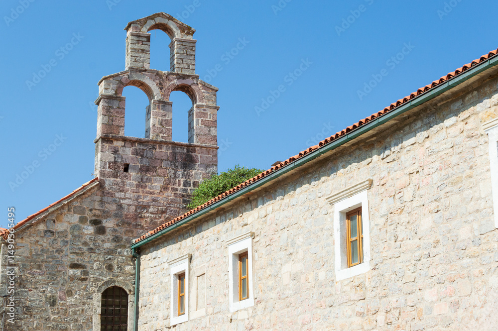 View of part of old stone house with tiled roof and window in old town against blue sky, medium shot View of part of old stone house with tiled roof and window in old town against blue sky, medium shot