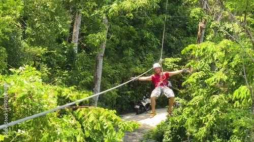A man is enjoying an exhilarating ride on a zip line that traverses the thick woods surrounding him