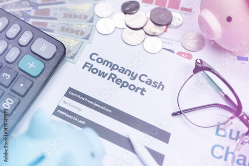 A company cash flow report surrounded by money, coins, a calculator, glasses, and a piggy bank on a desk.