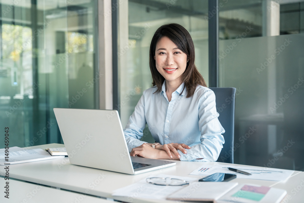 Portrait mature Asian it specialist business lady working on laptop pc sitting at desk in modern office smiling at camera. Middle-aged ceo bank manager woman using computer technology for work online Portrait mature Asian it specialist business lady working on laptop pc sitting at desk in modern office smiling at camera. Middle-aged ceo bank manager woman using computer technology for work online