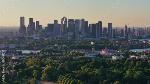 Close aerial descent over modern skyscrapers above lush city greenery in soft evening light