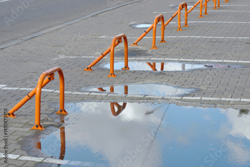 Row of folding parking barriers with lock on wet pavement after rain in reserved parking zone, with water puddles, securing reserved spot in public area with reflection and urban environment