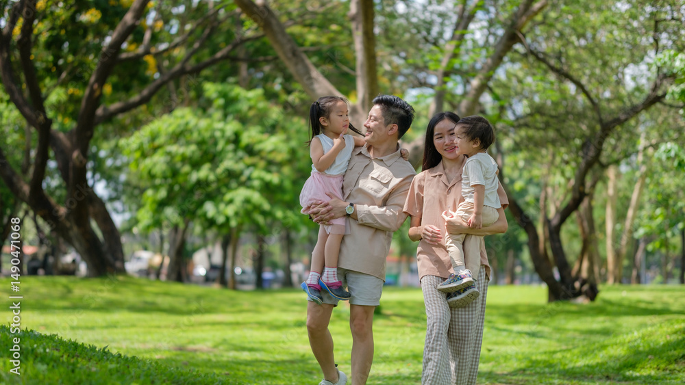 Fototapeta premium Happy Asian family walking together in a green park on a sunny day.