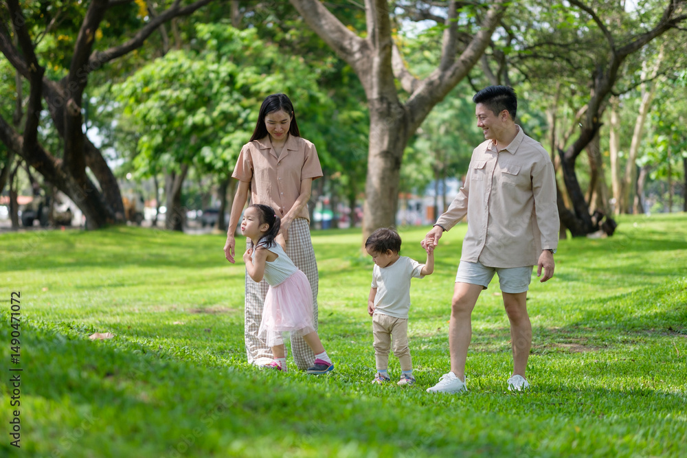 Obraz premium Happy Asian family walking together in a green park on a sunny day.