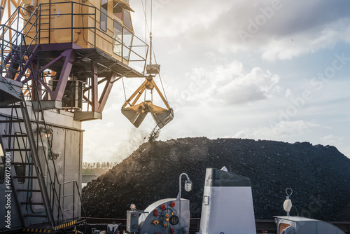 Foto Heavy crane loads coal onto a vessel at the port on a clear day by the river