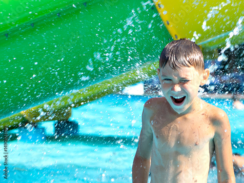 Joyful boy enjoying a splash of water at an aqua park. Bright summer day, excitement, and laughter captured in motion. Perfect image of childhood fun and outdoor recreation at a water slide