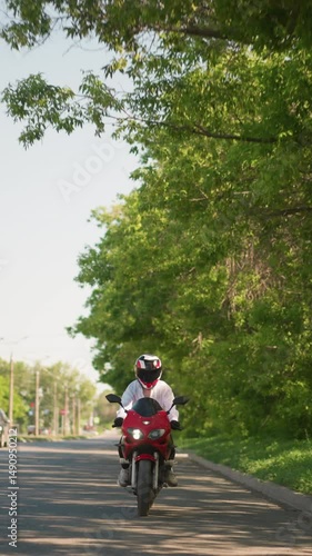 Wallpaper Mural A female motorcyclist rides a red power bike with one headlight on, passing near lush green trees in an urban setting, and cars pass closely by her, other vehicles can be seen on the other lane Torontodigital.ca