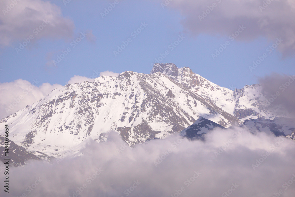 Obraz premium a cloud over a forest and a snowy mountain peak during sunset