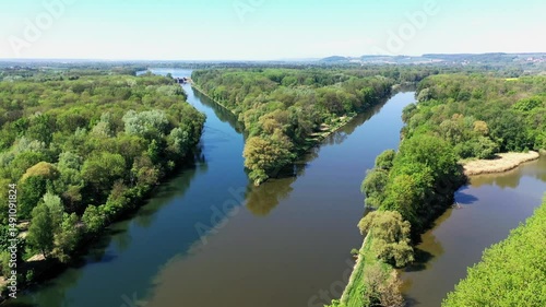 Die Lechmündung in die Donau zeigt eine friedliche Flusslandschaft mit üppiger Vegetation und klarem Wasser. Die Spiegelung der Bäume im Wasser und der blaue Himmel schaffen eine idyllische Atmosphäre