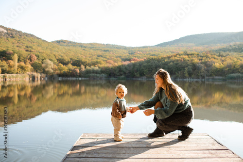 Young woman holding baby girl 1 year old wearing knitted sweaters over nature landscape view. Motherhood. Autumn season.