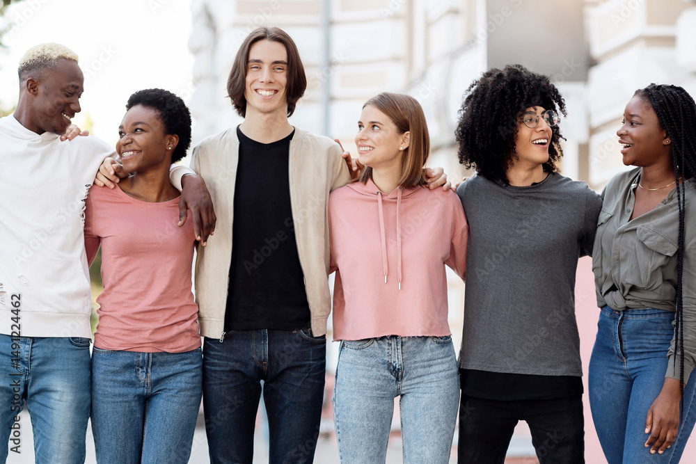 Obraz premium Friendship, community, team concept. Multiracial group of happy millennial men and women posing on the street, standing in a row, embracing and cheerfully smiling at camera, full length shot, panorama