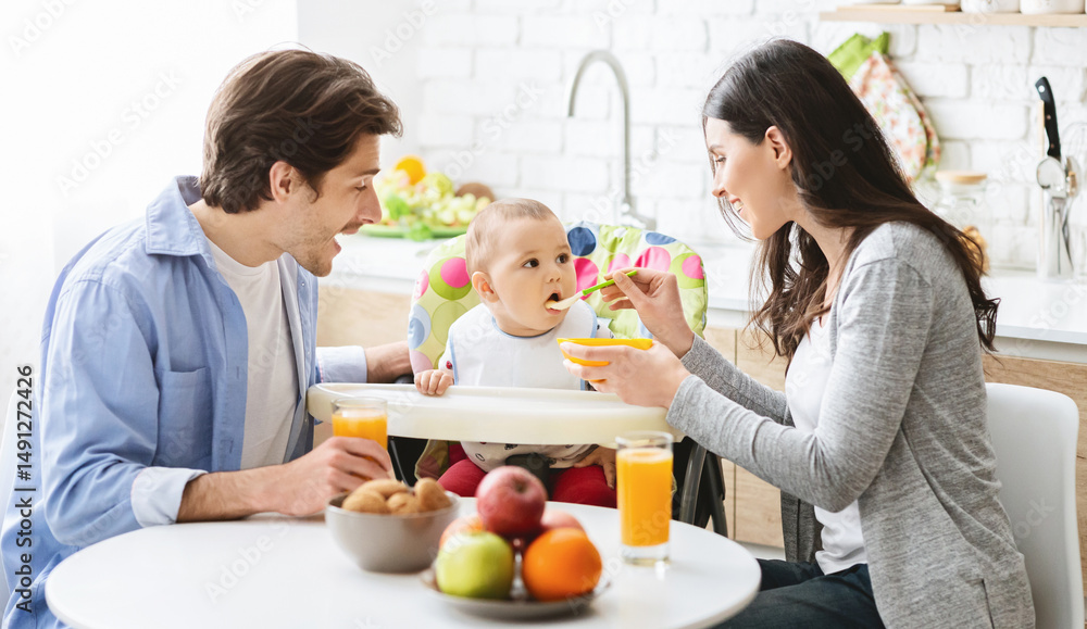 Good looking young family eating breakfast together with their baby son and feeding him Good looking young family eating breakfast together with their baby son and feeding him