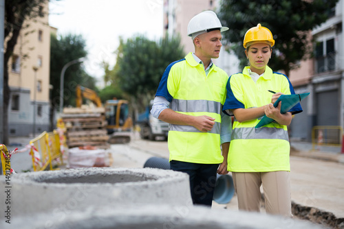 Two qualified engineers working on a construction site are discussing a construction plan, making important work notes