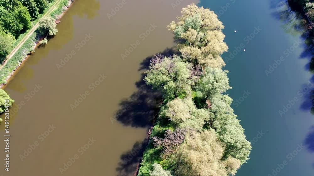 Die Lechmündung in die Donau zeigt eine friedliche Flusslandschaft mit üppiger Vegetation und klarem Wasser. Die Spiegelung der Bäume im Wasser und der blaue Himmel schaffen eine idyllische Atmosphäre