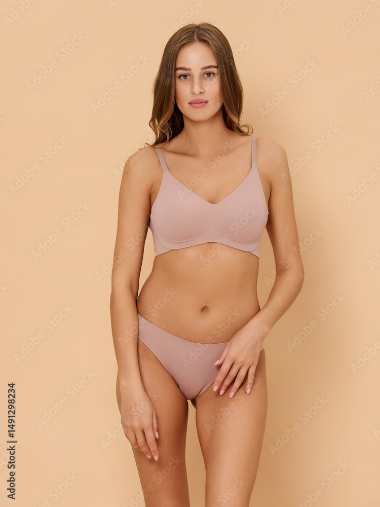 Fototapeta premium Girl model in underwear posing in studio on beige background.