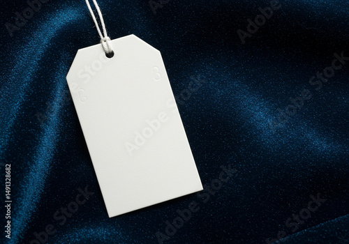 Blank white hang tag mockup on a dark blue silk or navy satin fabric. Great for premium apparel branding, sophisticated gift tags, or classic product presentations.