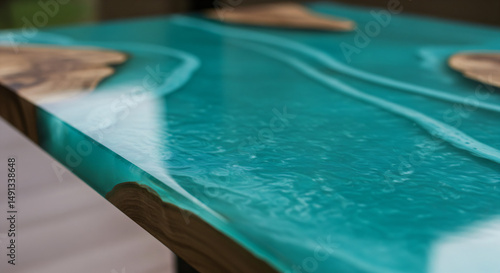 Close-up of a table with a turquoise epoxy resin surface. It has a glossy finish with flowing patterns, resembling water. Pieces of wood are embedded in the resin, adding a natural and artistic touch.